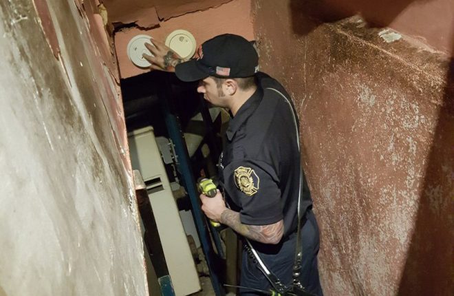 A Fire Department inspector checks a smoke detector.