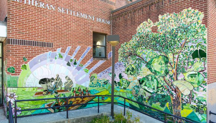 A vibrant mural depicting a purple sunrise and lush trees and plants growing as figures of people plant seeds.