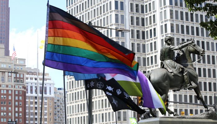 A rainbow flag with two additional stripes, one black and one brown, flies at City Hall. The Municipal Services building is in the background and a statue of a Civil War union general rides his horse nearby.