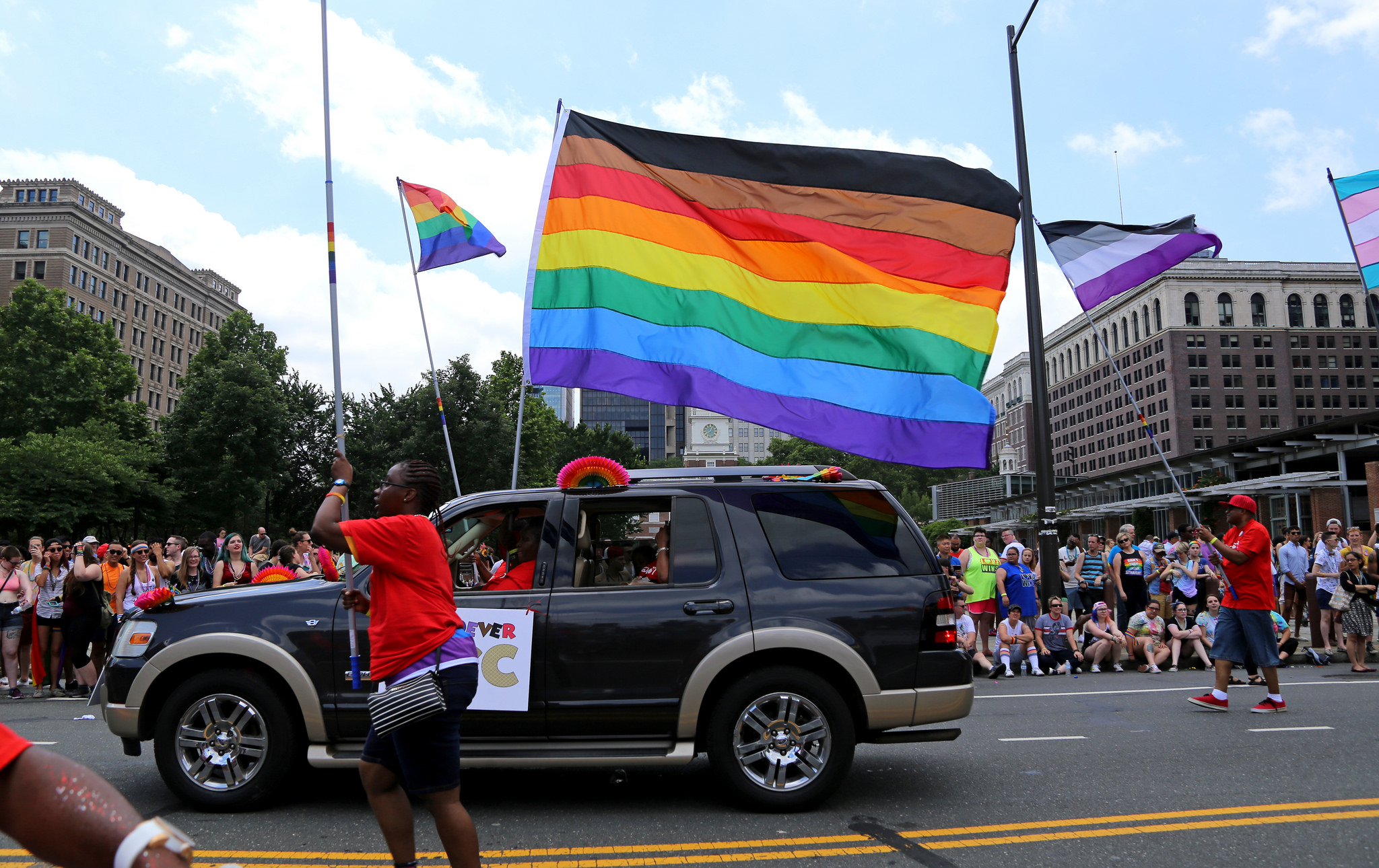 A truck drives in front of Independence Hall with a large LGBTQ flag with brown and black stripes on it representing LGBTQ people of color.