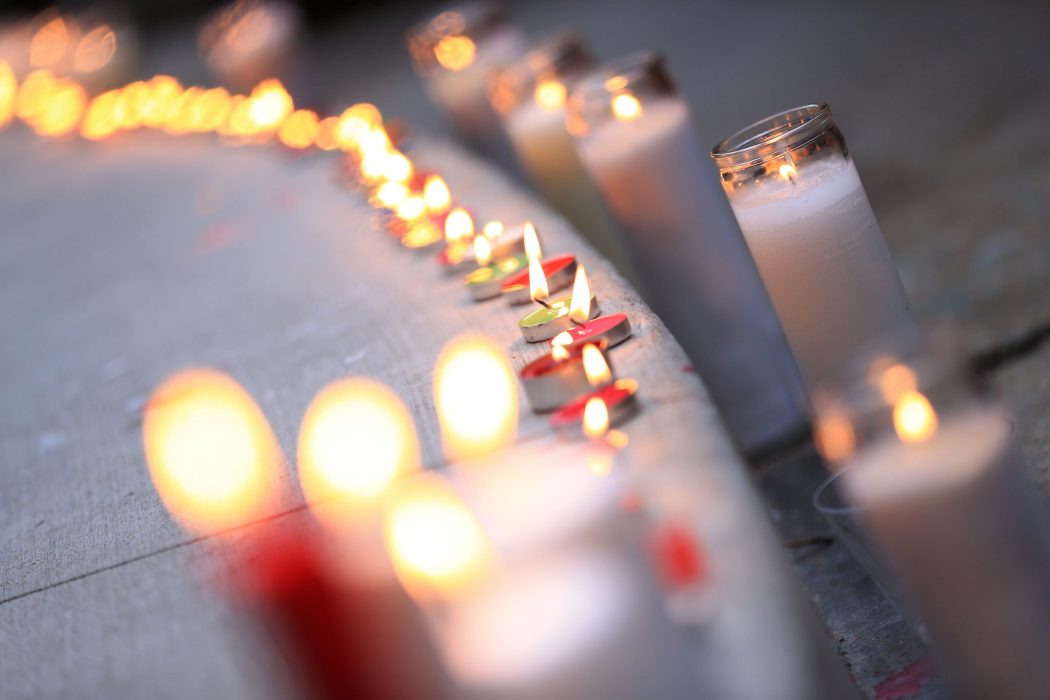A row of lit candles set on the sidewalk flicker at a vigil outside of City Hall.