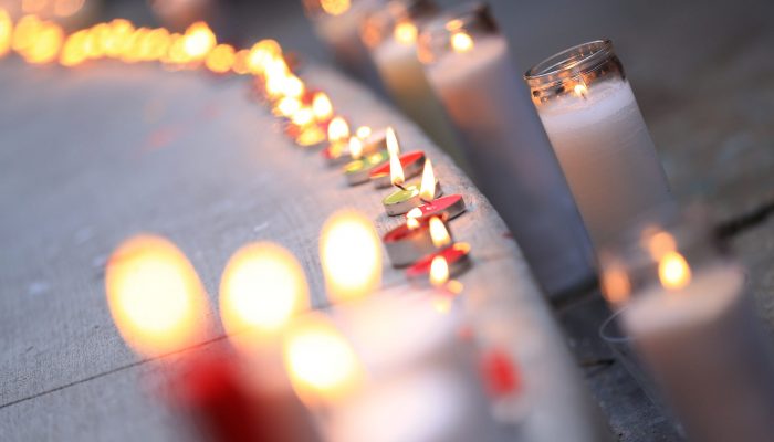 A row of lit candles set on the sidewalk flicker at a vigil outside of City Hall.