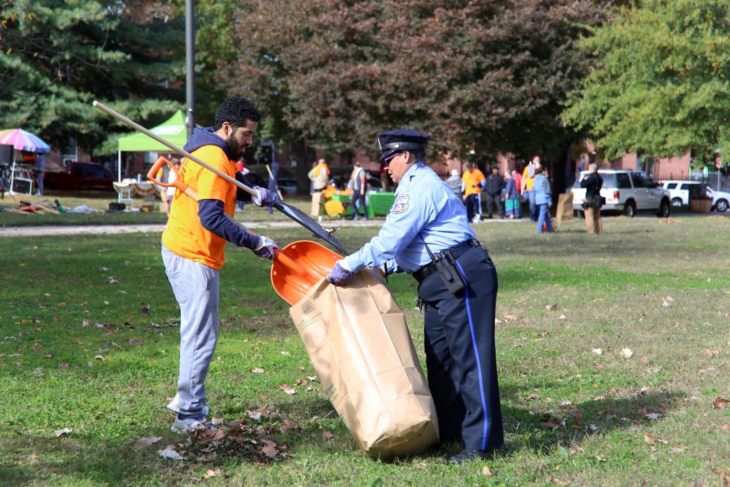 A volunteer puts trash and debris in a collection bag with the help of a Philadelphia police officer.