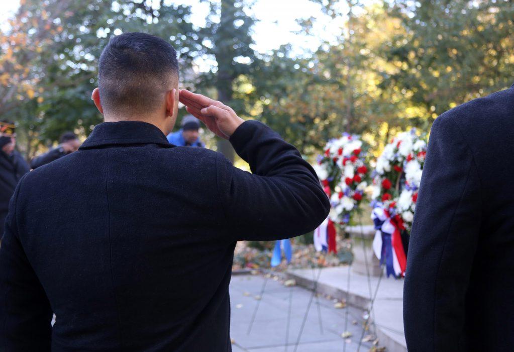 A man salutes the wreath on the Tomb of the Unknown Solider in Washington Square Park. Others stand solemnly in the background paying their respects.