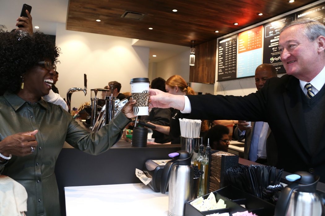 A cheerful Mayor Kenney hands a smiling customer her cup of coffee at a local coffee shop.