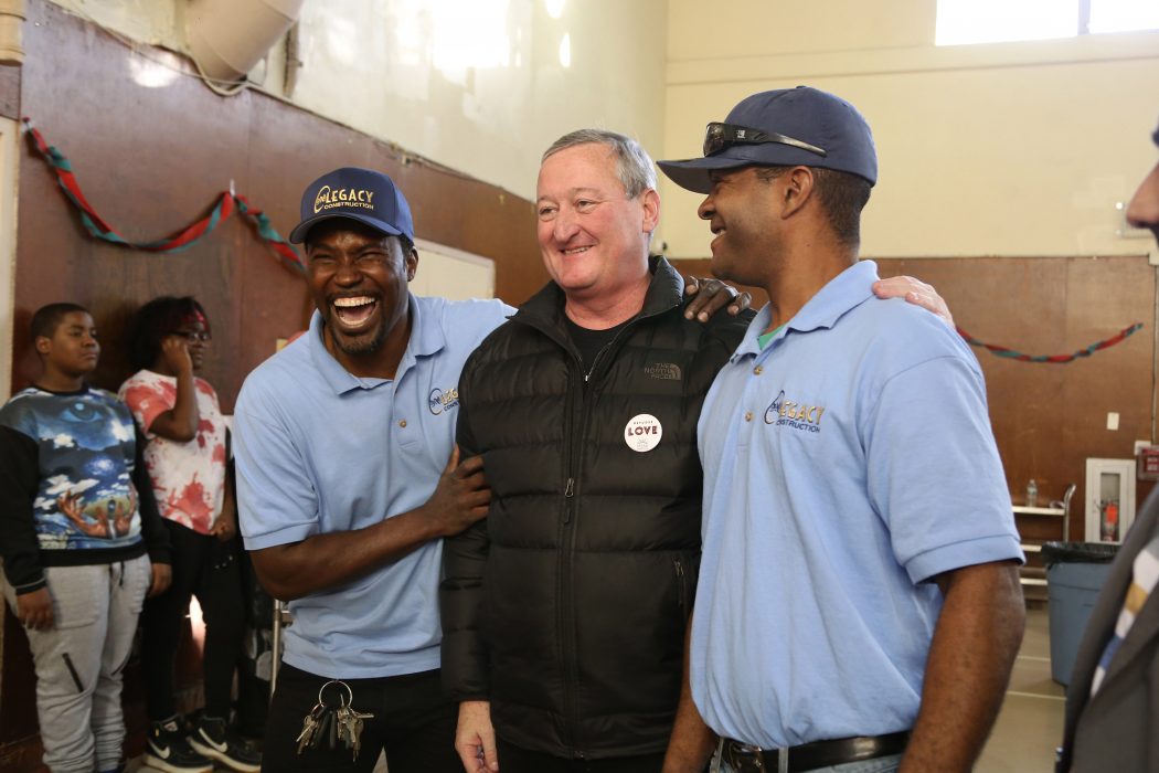 Mayor Kenney, standing between two attendees in matching uniforms, joins in the laughter at HIAS' annual Thanksgiving celebration for recently placed refugees. In the background others enjoy the festivities.