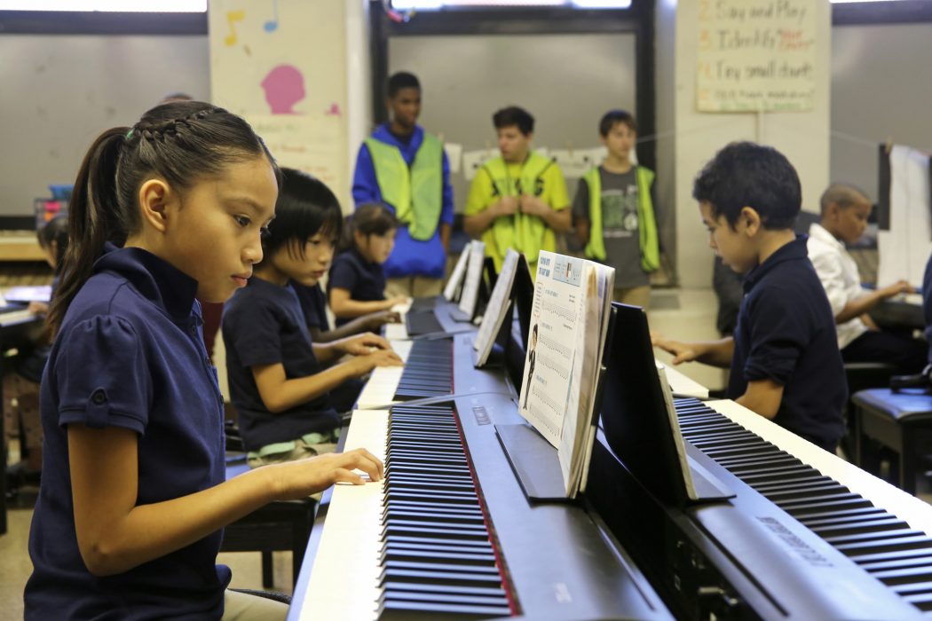 Young students in upper grades in elementary school or middle school sit at several keyboards playing music as part of a school music education program.