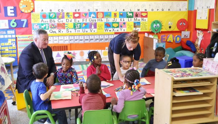Mayor Kenney and a diverse group of pre-schoolers sit around a table in their classroom. They excitedly work on their art projects as a teacher assists one of the children.