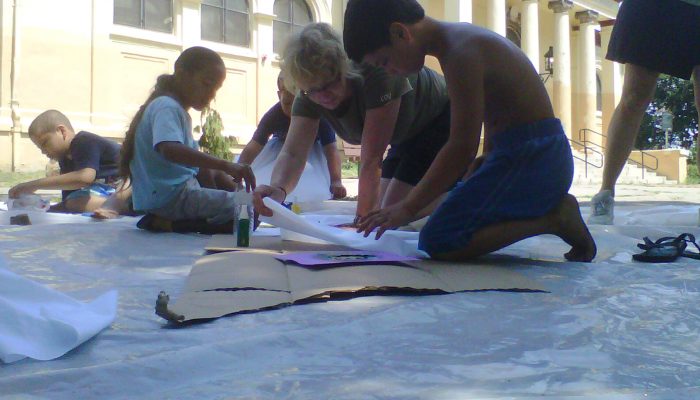 Children kneel on the ground and work on an art project.