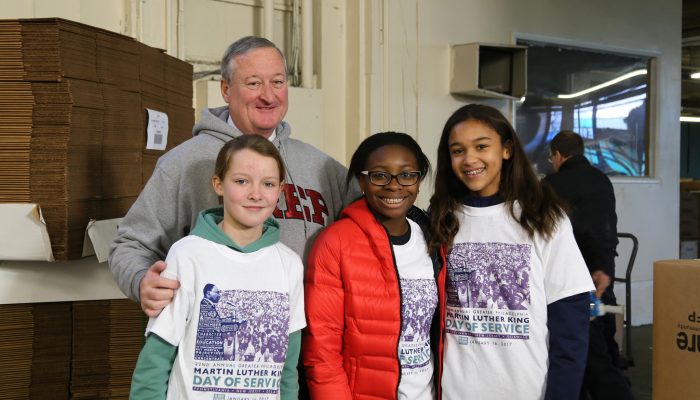 Mayor Kenney wears a hooded sweatshirt from St. Joseph's Prep as he stands with three middle- and high school-aged volunteers. Everyone is smiling happily. They all just volunteered.