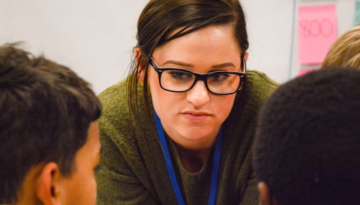 White woman wearing glasses bends down to listen to two young men.