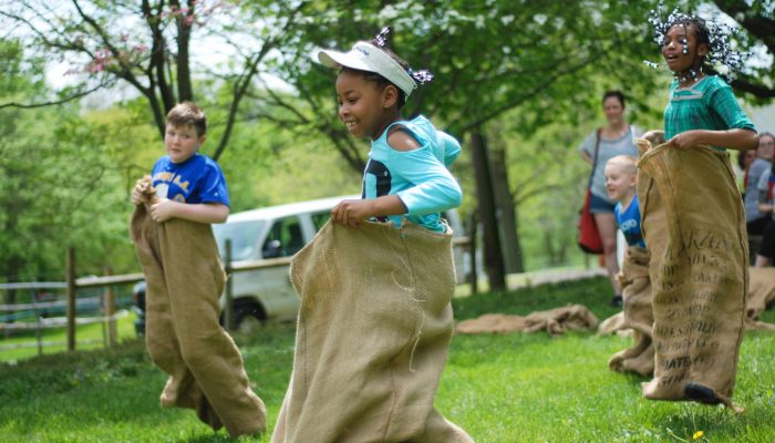 Children laugh as they sack race across a lawn.