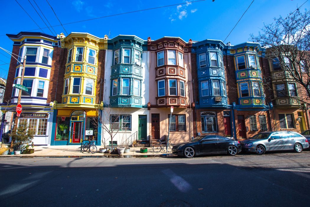 Identical three-story row homes in Queen Village are all exactly the same except they are each different colors that contrast with each other showing that while each house is the same it is also different.