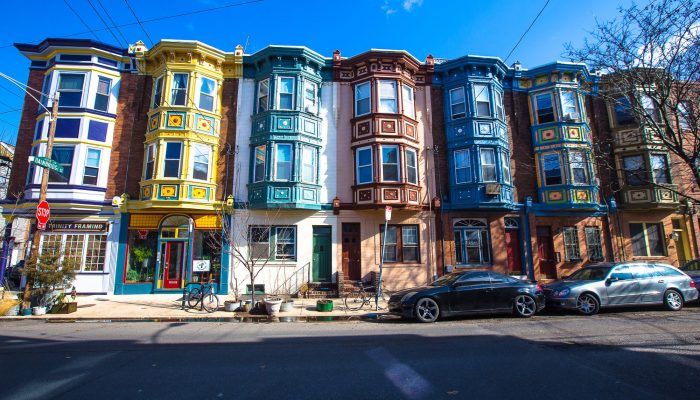 Identical three-story row homes in Queen Village are all exactly the same except they are each different colors that contrast with each other showing that while each house is the same it is also different.