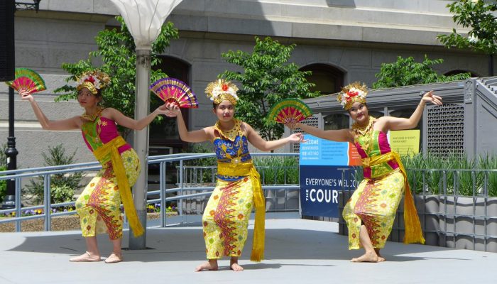 Three women dance in beautiful, bejeweled outfits in City Hall's courtyard. There are flowers around and the entrance to the Broad Street Line subway is nearby.