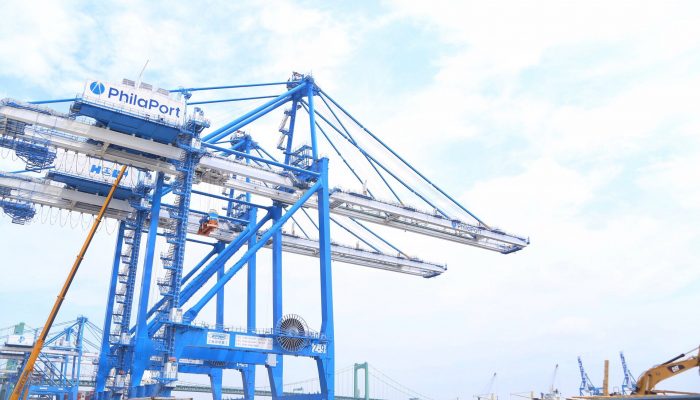 A massive set of two cranes larger than a city building rises from the shoreline of the Delaware River. They are metal and evoke industry.