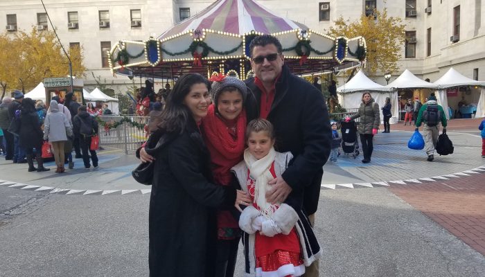 maria poses with her family in front of a carousel