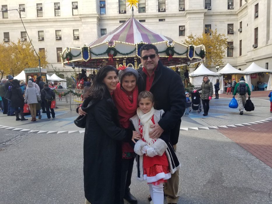 maria poses with her family in front of a carousel