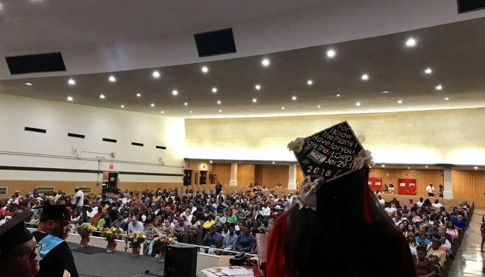 A graduate stands on stage delivering a captivating speech overlooking the crowd.