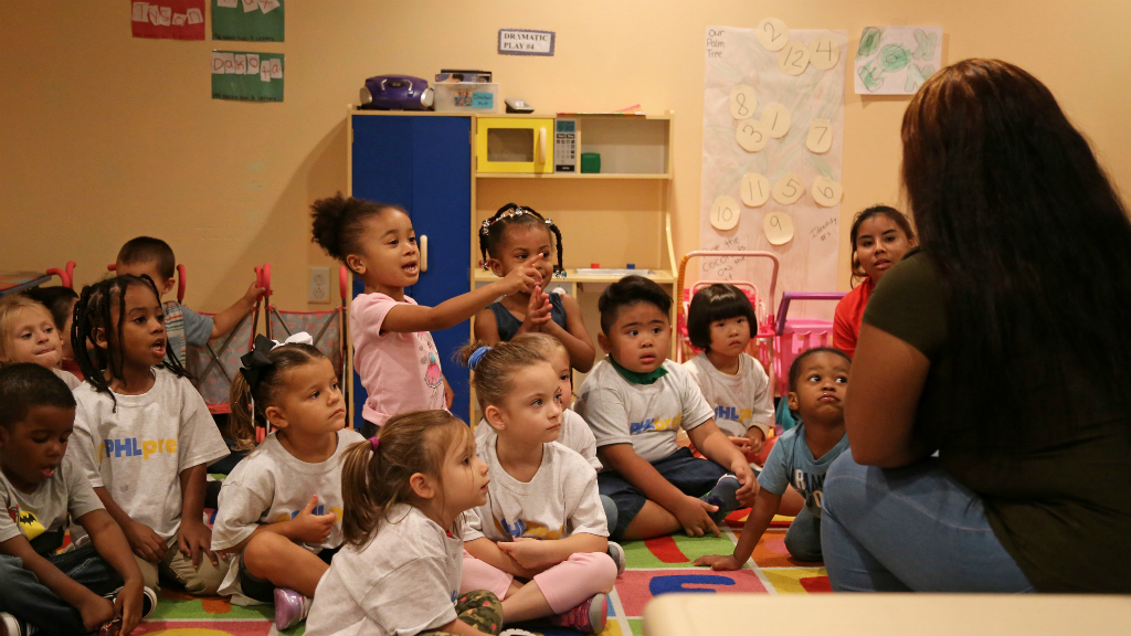 Philadelphia school children sit on a rug and listen to their teacher read a story