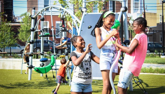 Children of various ages smiling and playing in a brand new playground in a Philly neighborhood.