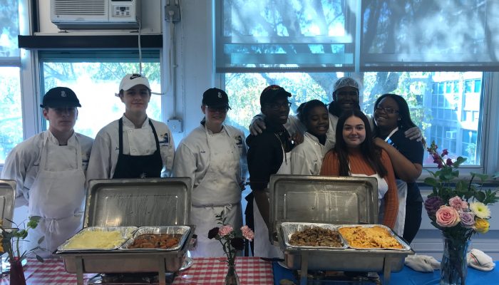 Culinary arts students stand behind a table in front of food they've made with flowers and smile