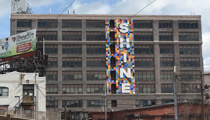 A colorful mural on an old building says 'Shine'.