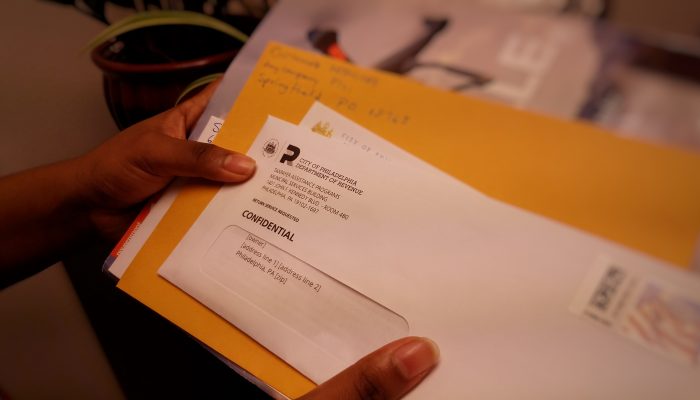 A woman holds a stack of mail that includes a notice letter from the Philadelphia Department of Revenue