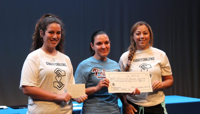 2 young women awarding a check to a nonprofit representative