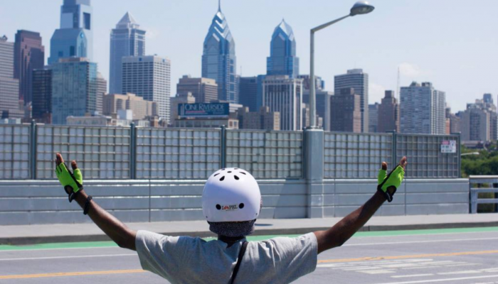 Person in a helmet looks at the city skyline and raises their arms over their head.