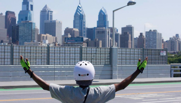 La persona con casco mira el horizonte de la ciudad y levanta los brazos por encima de la cabeza.