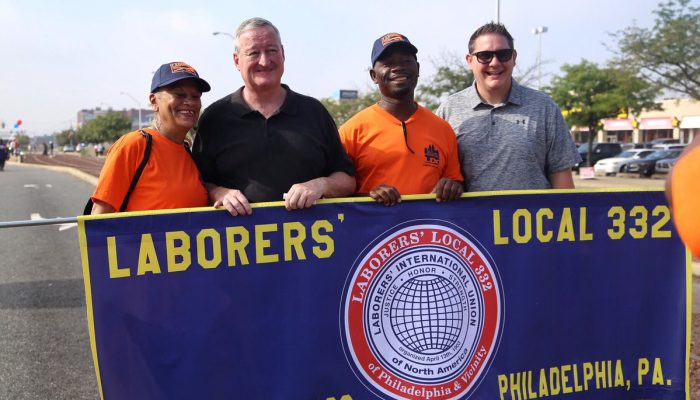 Mayor Kenney standing along members of the Laborers' Union and Deputy Mayor for Labor Rich Lazer while they hold a union banner at the Labor Day parade.