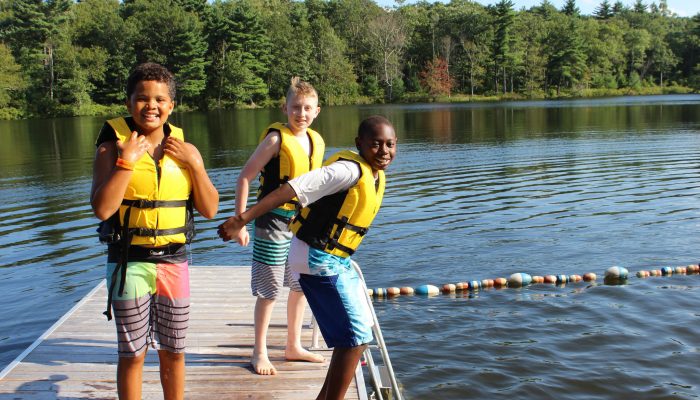 Three male swimmers get ready to jump in a lake.