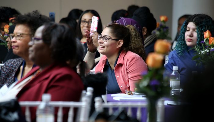 woman with glasses smiling at a table surrounded by other women