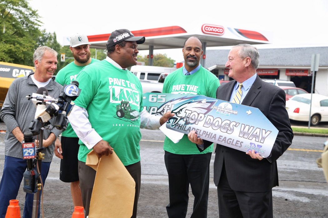 The Mayor standing alongside Streets Commissioner Carlton Williams while holding up a street sign that says "Top Dogs' Way"