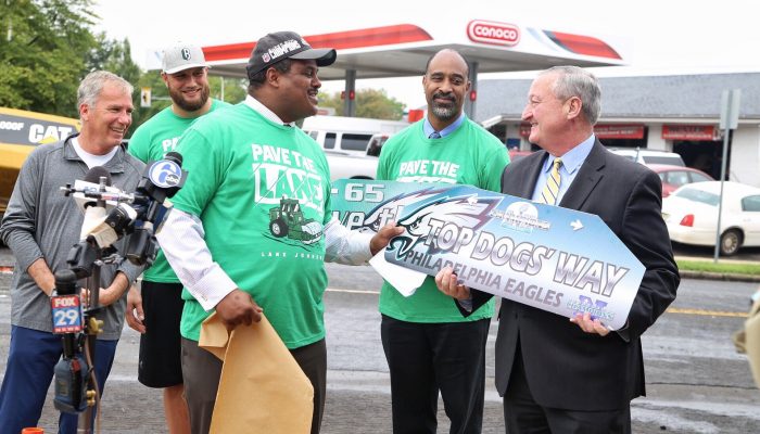 The Mayor standing alongside Streets Commissioner Carlton Williams while holding up a street sign that says "Top Dogs' Way"