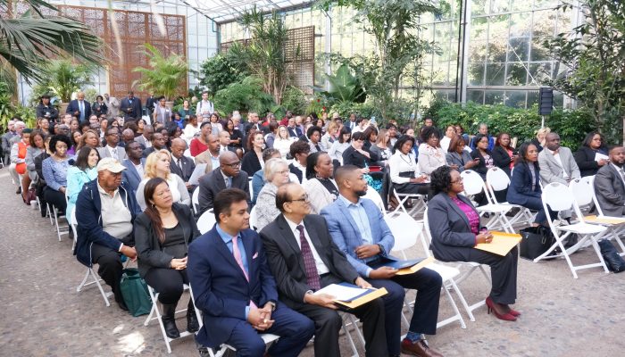 Diverse crowd sits in chairs surrounded by greenery at the Fairmount Park Horticulture Center.