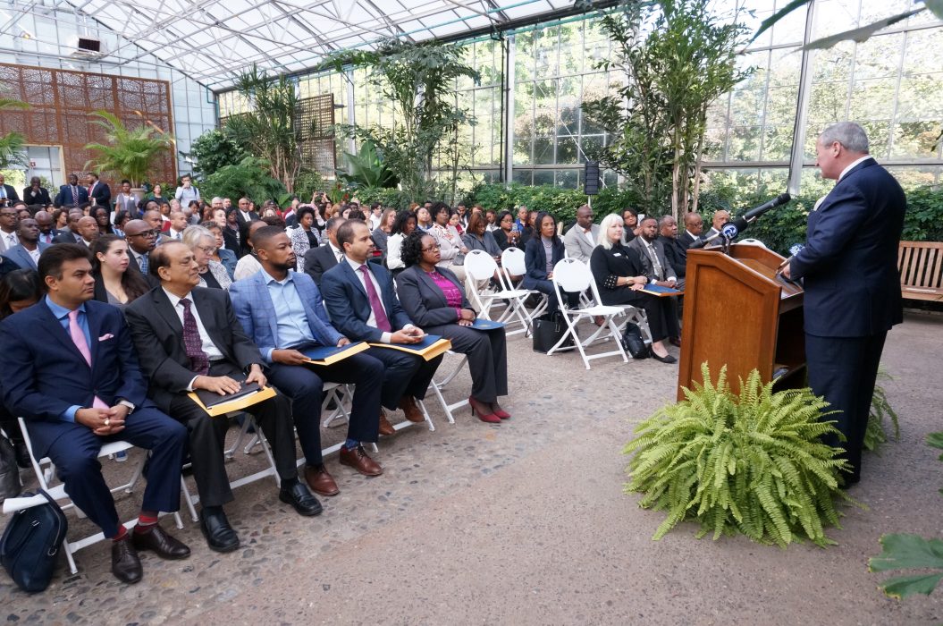 Diverse crowd sits in chairs surrounded by greenery at the Fairmount Park Horticulture Center.