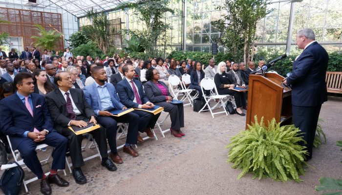 Diverse crowd sits in chairs surrounded by greenery at the Fairmount Park Horticulture Center.