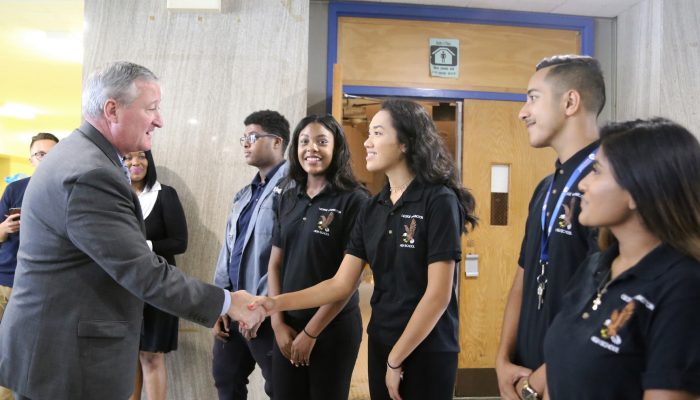 肯尼市长与社区学校乔治华盛顿高中的学生握手，他们都笑了起来。