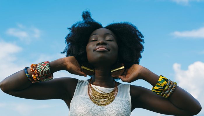 Une femme sourit les yeux fermés. Le fond est un ciel bleu clair.