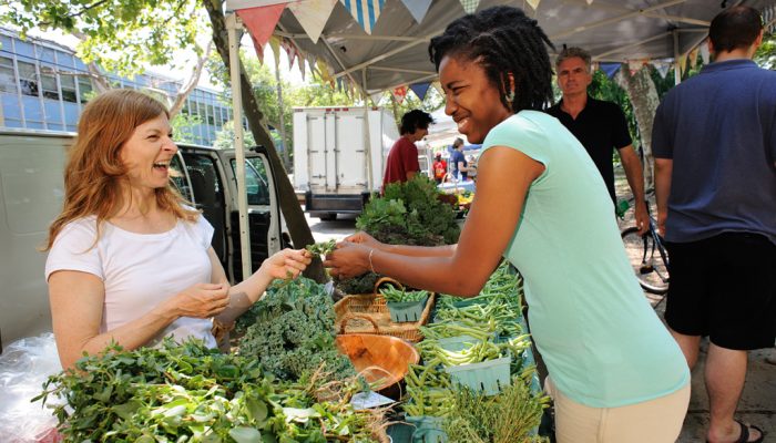 Two women laugh over produce.