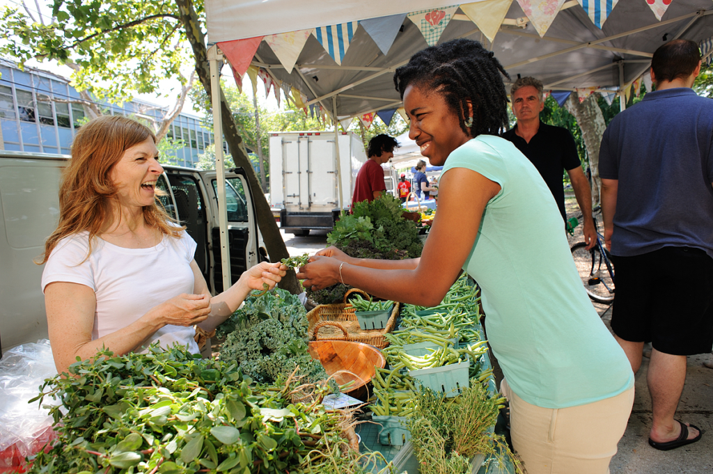 Two women laugh over produce.