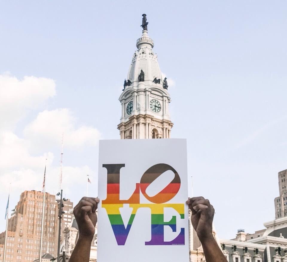 hands holding up a rainbow love sign in front of city hall