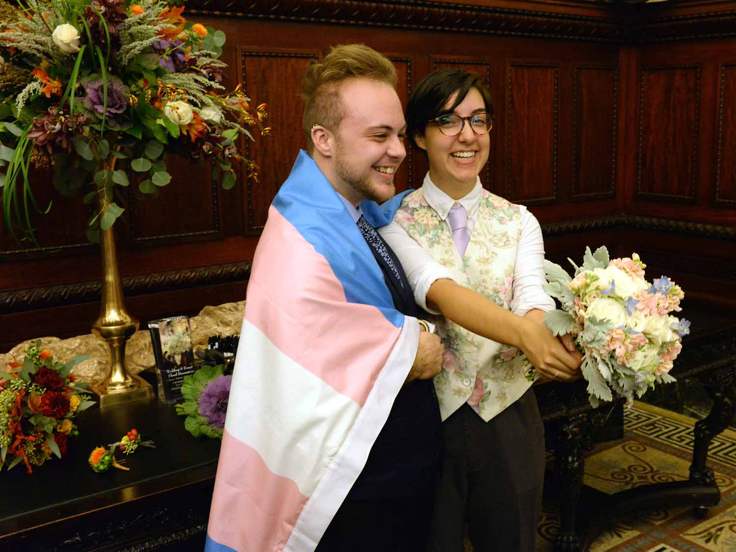 couple getting married smiles with a tran pride flag wrapped around them