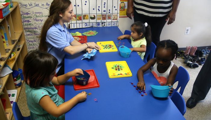 A pre-K instructor sits with students, teaching them how to count