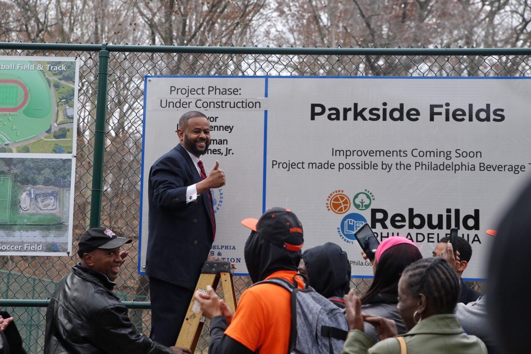 Councilman Curtis Jones, Jr., giving a thumbs up after adding a sign that reads, "Under Construction," at Parkside Fields. The sign says that Rebuild is made possible by the Philadelphia Beverage Tax.