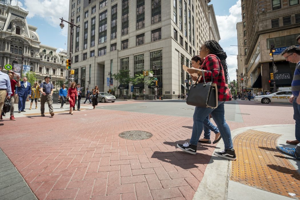 People walking across the new ADA improvements on South Broad Street where the sidewalk seamlessly melds into the street instead of being a curb.