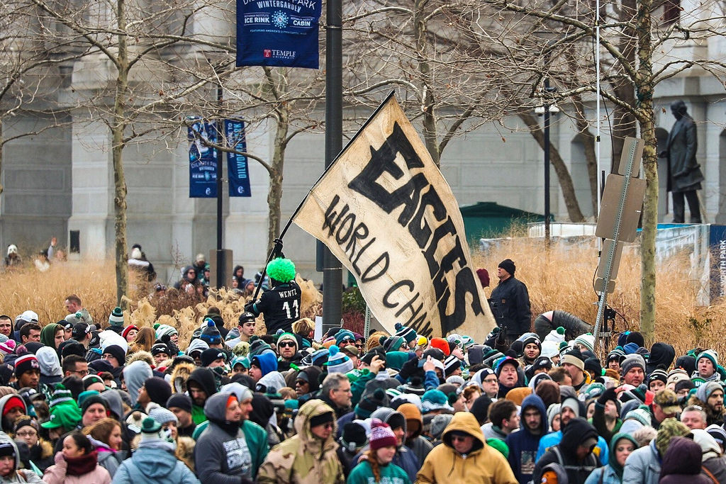 A man in a neon green wig waving a homemade flag that says "Eagles World Champs" amid a crowd of thousands in front of City Hall during the Eagles Super Bowl victory parade in February 2018.