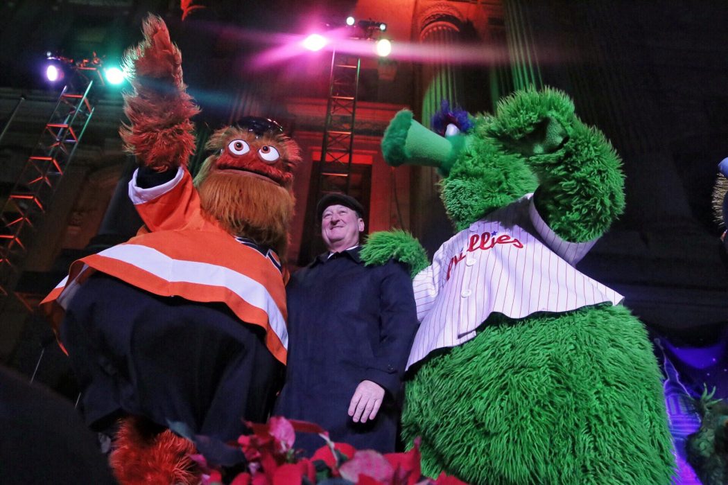 Flyers masdcot Gritty and the Phillie Phanatic standing next to Mayor Kenney at City Hall's holiday tree lighting in 2018.